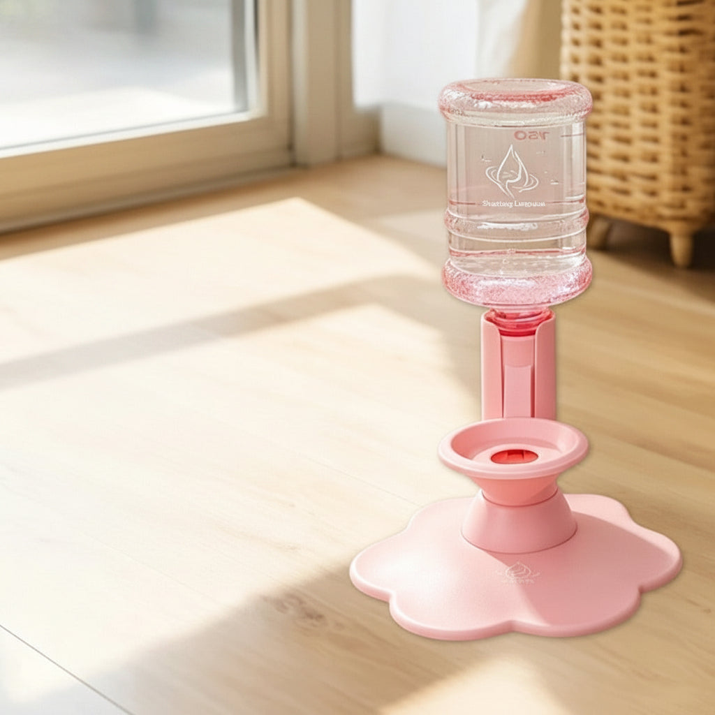 Pink automatic cat water dispenser with a clear bottle, shown on a wooden floor with an inset product kit list. The kit includes a pink dispenser, a clear bottle, a Velcro hook, a suction cup, a cleaning brush, a straw, and transparent stickers.