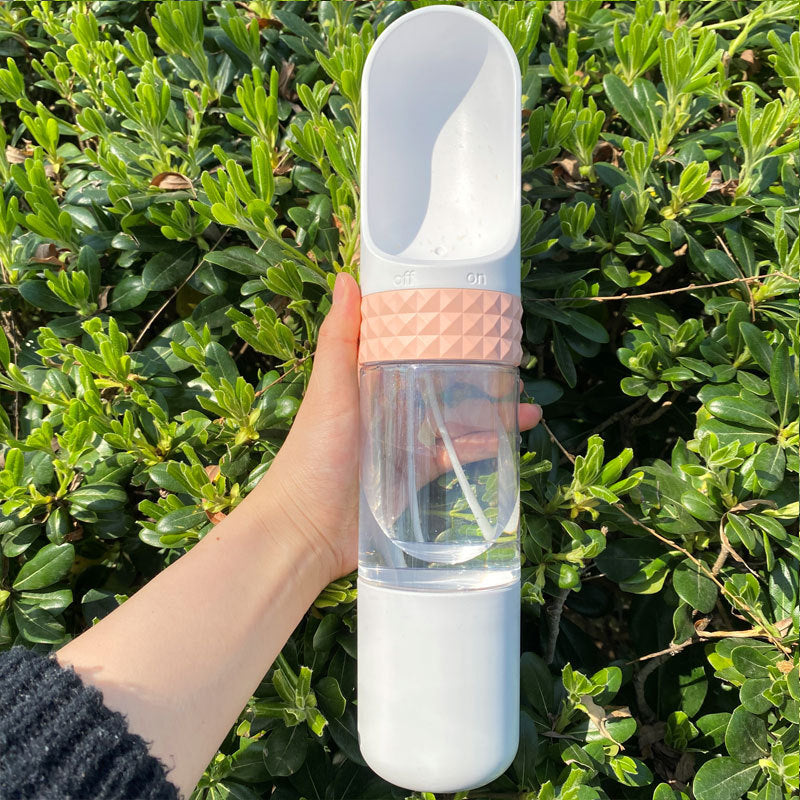 Hand holding a clear water bottle with pink and white accents against a green leafy background